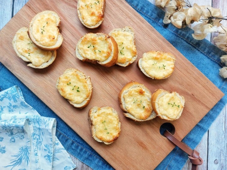 Torradinhas de maionese e queijo servidas em uma tábua.