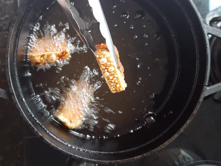 Uma panela com óleo quente e torresmos.