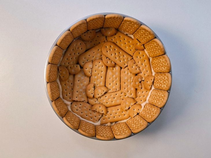 Biscoitos sendo rapidamente mergulhados no leite e acomodados no fundo da forma.