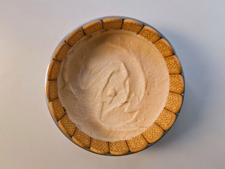 Camada de creme sendo espalhada sobre os biscoitos cobrindo toda a superfície.