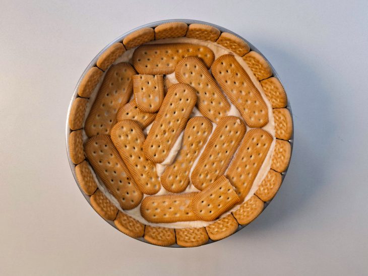 Montagem sendo repetida com novas camadas de biscoito e creme até preencher a forma.