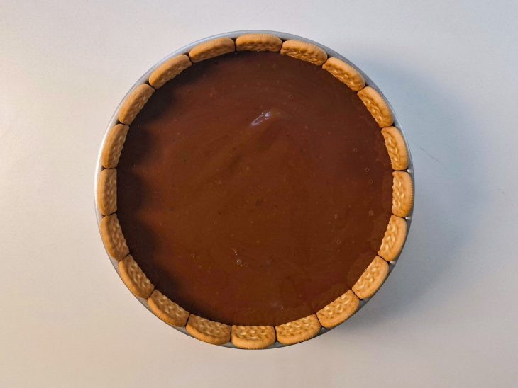 Ganache sendo espalhada por cima da torta com espátula, nivelando a superfície.