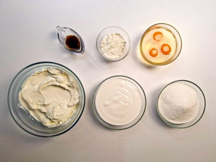 Ingredientes organizados com potes de cream cheese, creme de leite, açúcar, ovos e farinha.