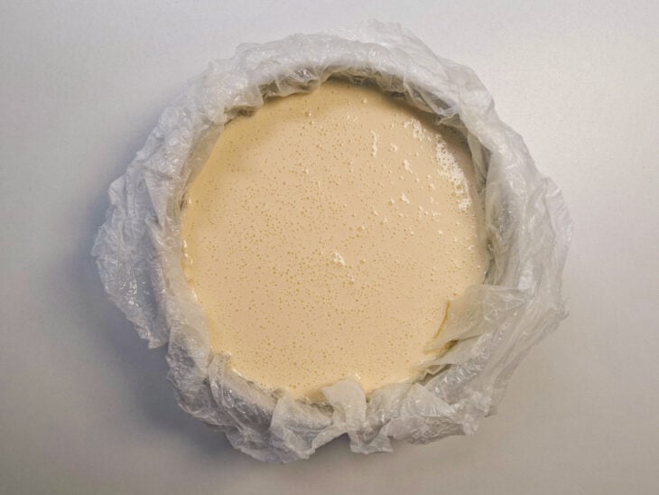 Massa homogênea e fluida sendo vertida na forma redonda forrada com papel-manteiga enrugado.