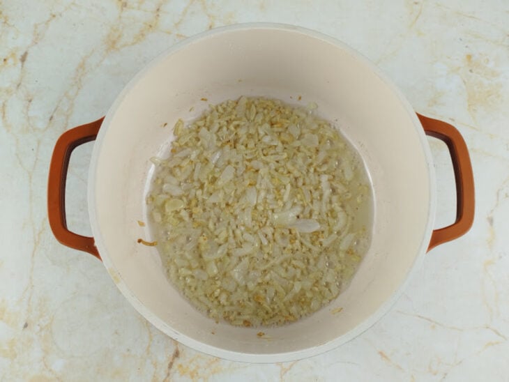 Cebola sendo cortada em cubos, alho picado, tomate e palmito preparados para a receita.