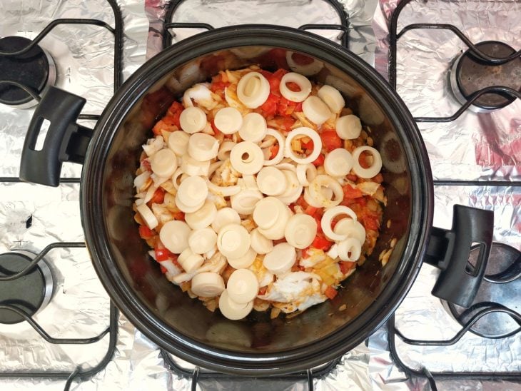 Uma panela refogando alho, cebola, temperos, tomate, bacalhau e bacalhau.