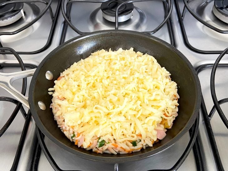 Uma frigideira contendo a mistura de arroz coberta com queijo.