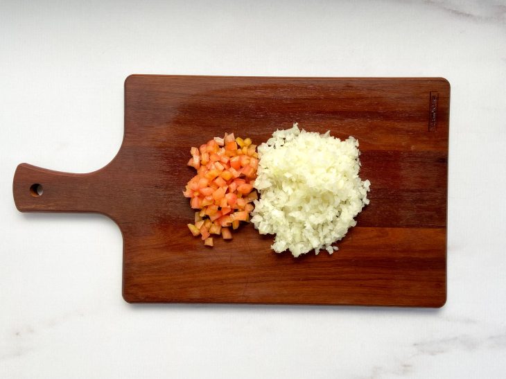 Tábua com tomate e cebola cortados em cubos pequenos.