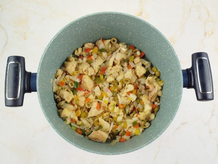 Legumes, bacalhau e temperos sendo refogados na panela até ficarem macios.