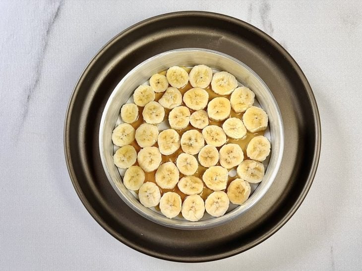 Caramelo e bananas em rodelas posicionadas sobre o fundo de uma forma redonda.