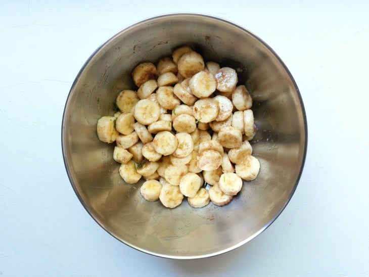 Um recipiente contendo rodelas de bananas temperadas com as raspas, o suco de limão e a canela.