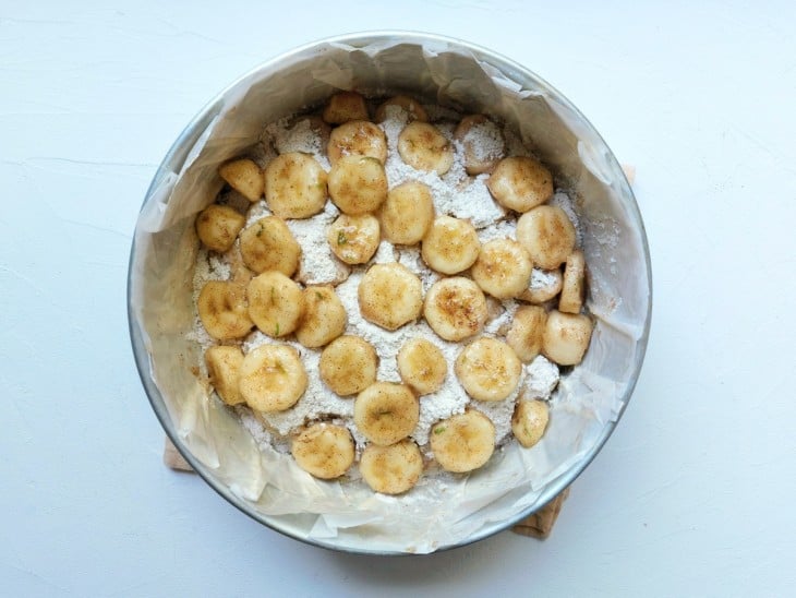 Uma forma redonda forrada contendo rodelas de banana cobertas com farofinha.
