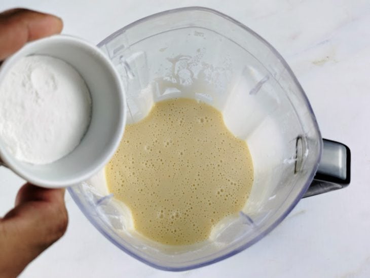 Um liquidificador com leite, ovos, açúcar, farinha e fermento sendo adicionado.