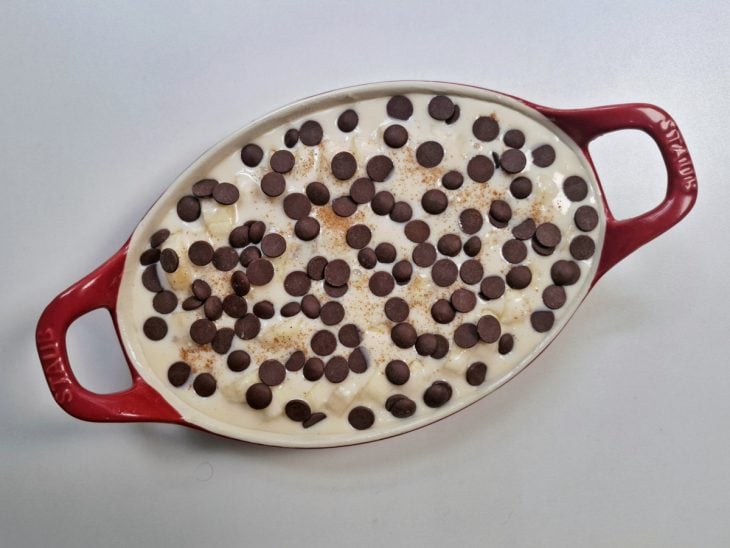 Mistura despejada no refratário, canela salpicada e gotas de chocolate colocadas por cima.