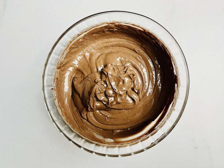 Creme de leite e chocolate em pó misturados em uma tigela de vidro.