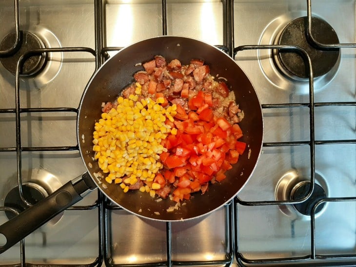 tomate e milho sendo adicionados a frigideira com calabresa, alho e cebola.