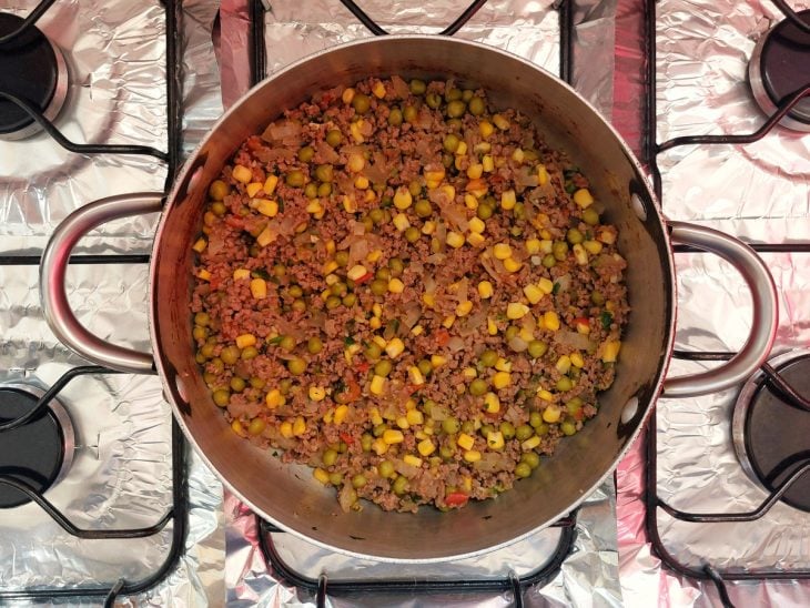 Uma panela refogando alho, cebola, carne moída, tomate, milho e ervilhas.