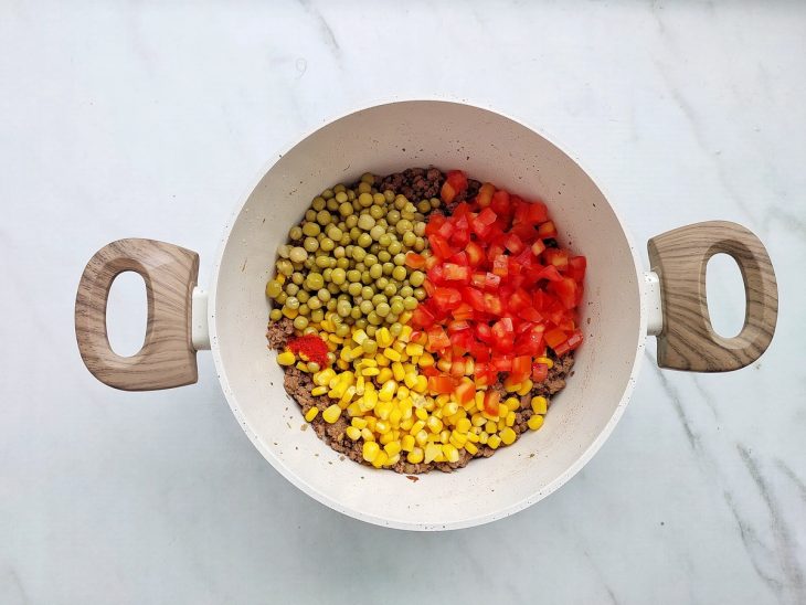 Legumes e temperos sendo misturados ao recheio na panela.