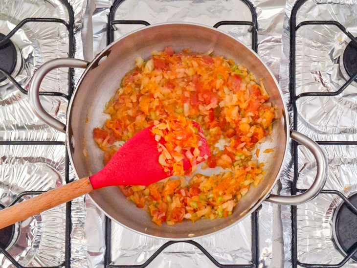 Alho dourando no azeite com legumes refogando até ficarem macios e levemente brilhantes.