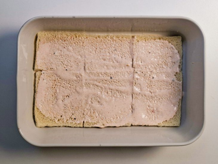 Base formada com fatias de pão alinhadas e levemente umedecidas com molho.