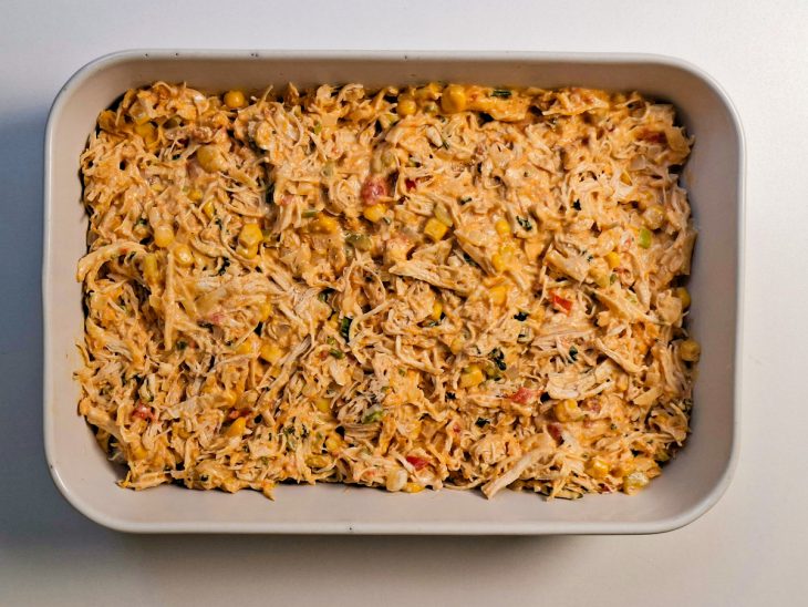 Recheio de frango espalhado e nivelado com espátula sobre a camada de pão.