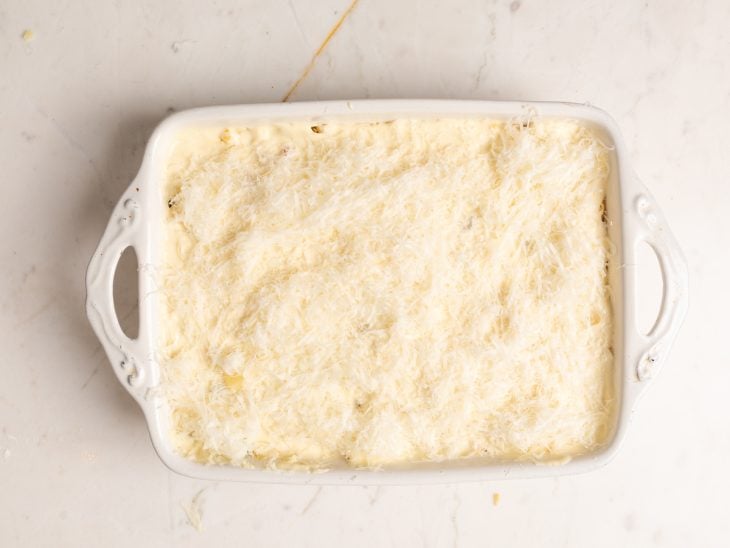Restante da massa despejada e coberta por queijo parmesão salpicado.