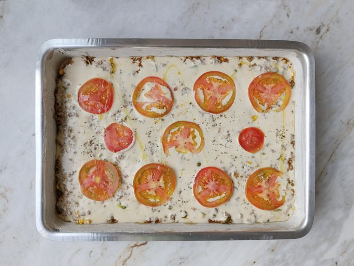 Torta decorada com tomate, orégano e fio de azeite antes de assar.