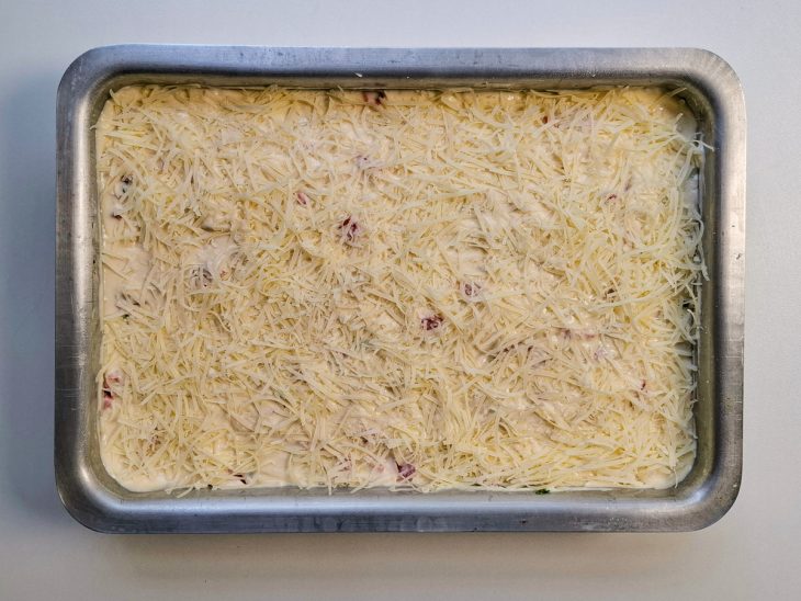 Com recheio posto, a segunda metade da massa é despejada, parmesão finaliza por cima.