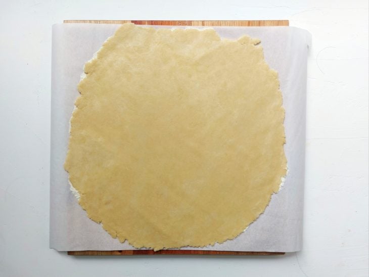 Uma bancada, forrada com papel manteiga, com uma parte da massa aberta.