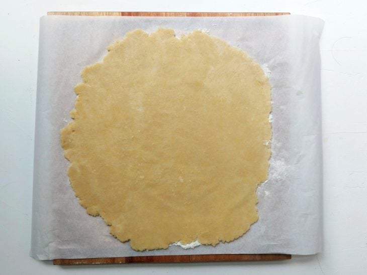Uma bancada, forrada com papel manteiga, com uma parte da massa aberta.