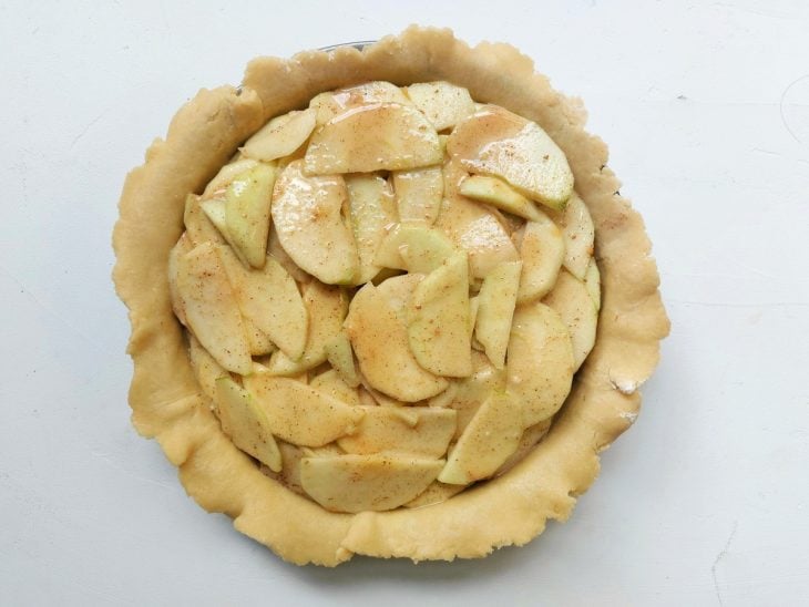 Uma forma redonda forrada com uma massa e recheada com as fatias de maçã.