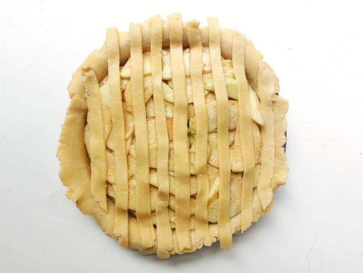 Uma forma redonda forrada com uma massa, recheada com as fatias de maçã e cobertas com tiras de massa.