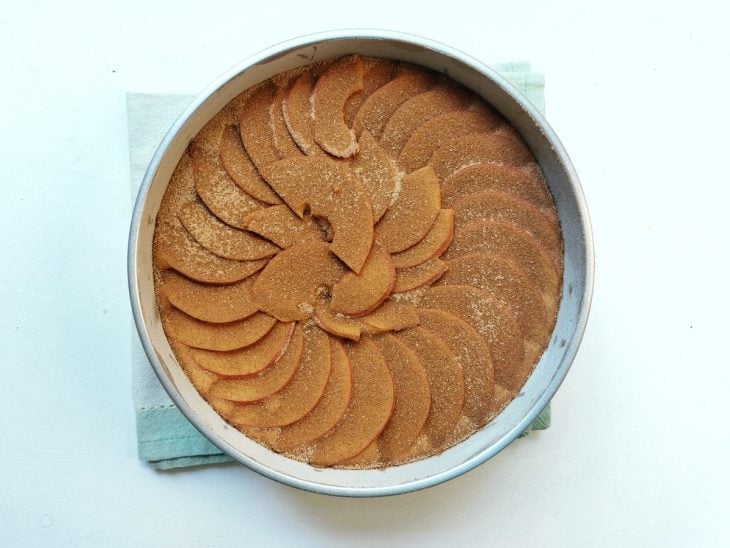 Uma forma contendo massa de bolo de maçã coberta com fatias de maçãs e canela.