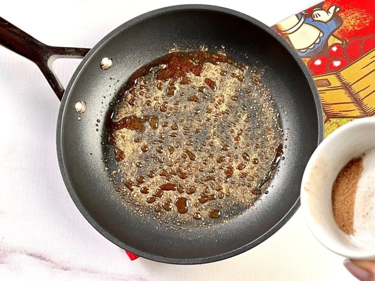 Uma frigideira contendo manteiga derretida com açúcar demerara e canela salpicados.