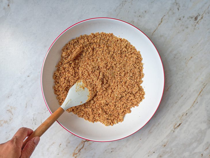 Na tigela, água adicionada a mistura de bolacha triturada e manteiga.