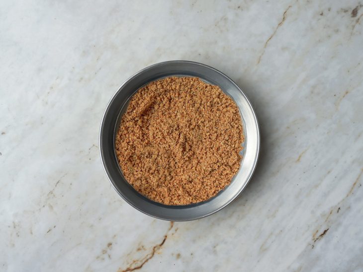 Numa forma, a farofa da bolacha distribuída no fundo.