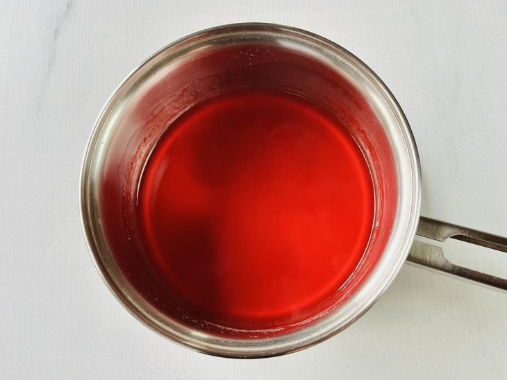 Água, açúcar, amido e gelatina de morango misturados em uma panela.