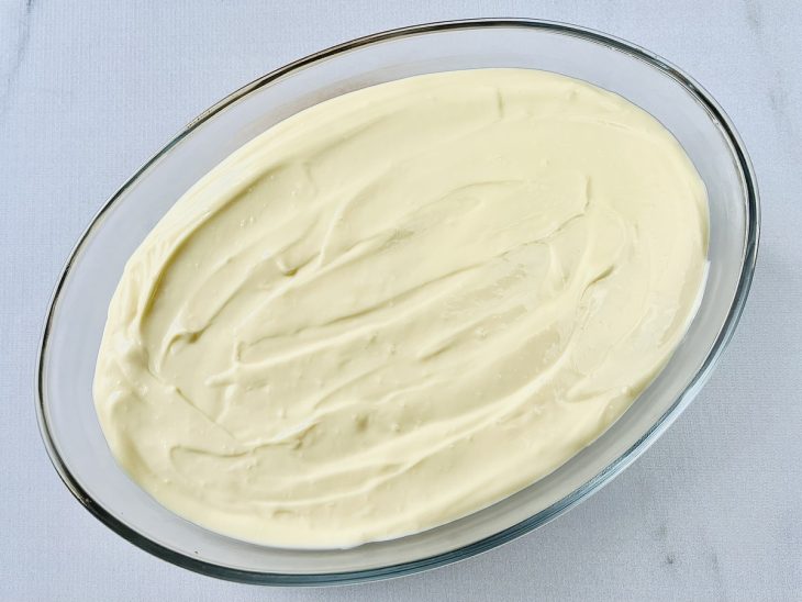 Creme de baunilha espalhado sobre a base de bolacha na travessa de vidro.