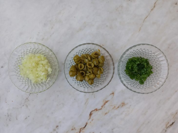 Cebola, azeitonas e cheiro-verde picados em recipientes de vidro.