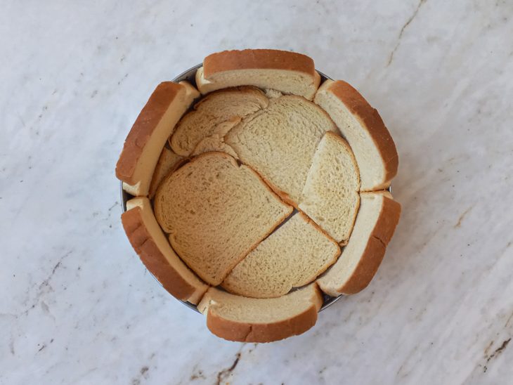 Fatias de pães de forma forrando uma forma redonda.