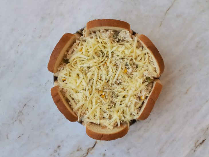 Camadas de pão, recheio de frango, queijo mussarela e orégano adicionados a forma.
