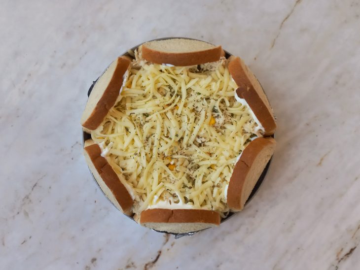 Requeijão espalhado sobre as bordas de pão da torta.