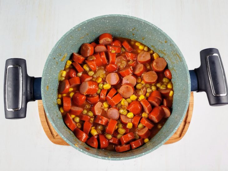 Milho, ervilha, tomate e salsichas refogados na panela.