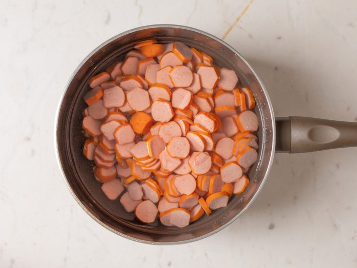 Salsichas cortadas em rodelas numa panela com água.