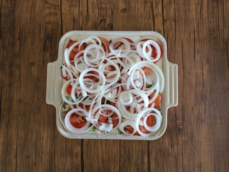 Cebolas e tomates em rodelas acomodados por cima da torta.