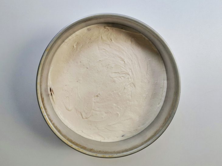 Creme branco despejado sobre a base de bolacha na forma.