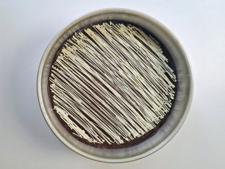 Ganache de chocolate ao leite adicionado a forma e ganache de chocolate branco decorando por cima.