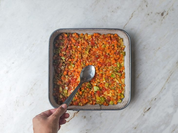 Recheio colorido de legumes distribuído sobre a primeira camada de massa.
