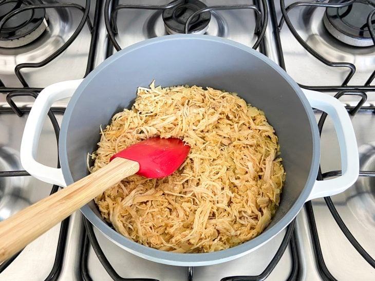 Frango desfiado colocado na panela com o alho e cebola fritos.