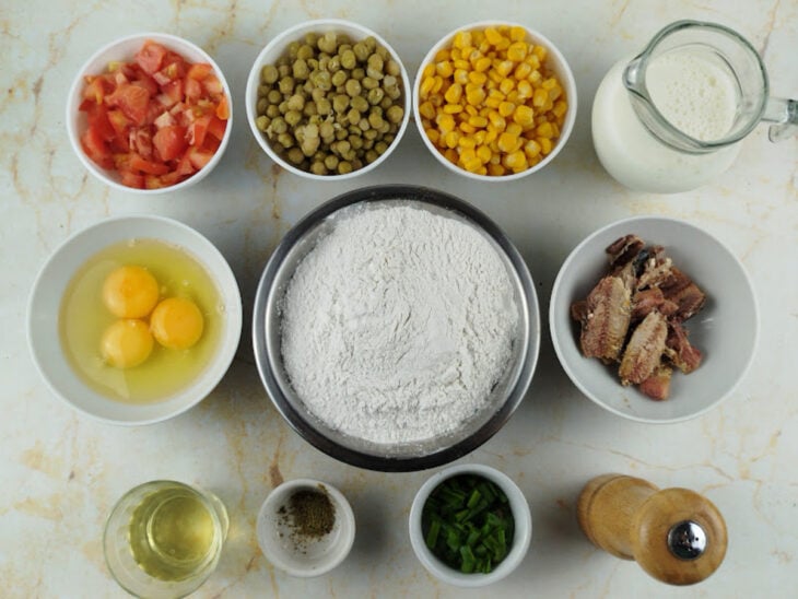 Ingredientes organizados na bancada com legumes picados, sardinha e ingredientes da massa separados.